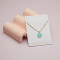 Gold necklace with a turquoise pendant on a 'Foxy Originals' card against a pink background