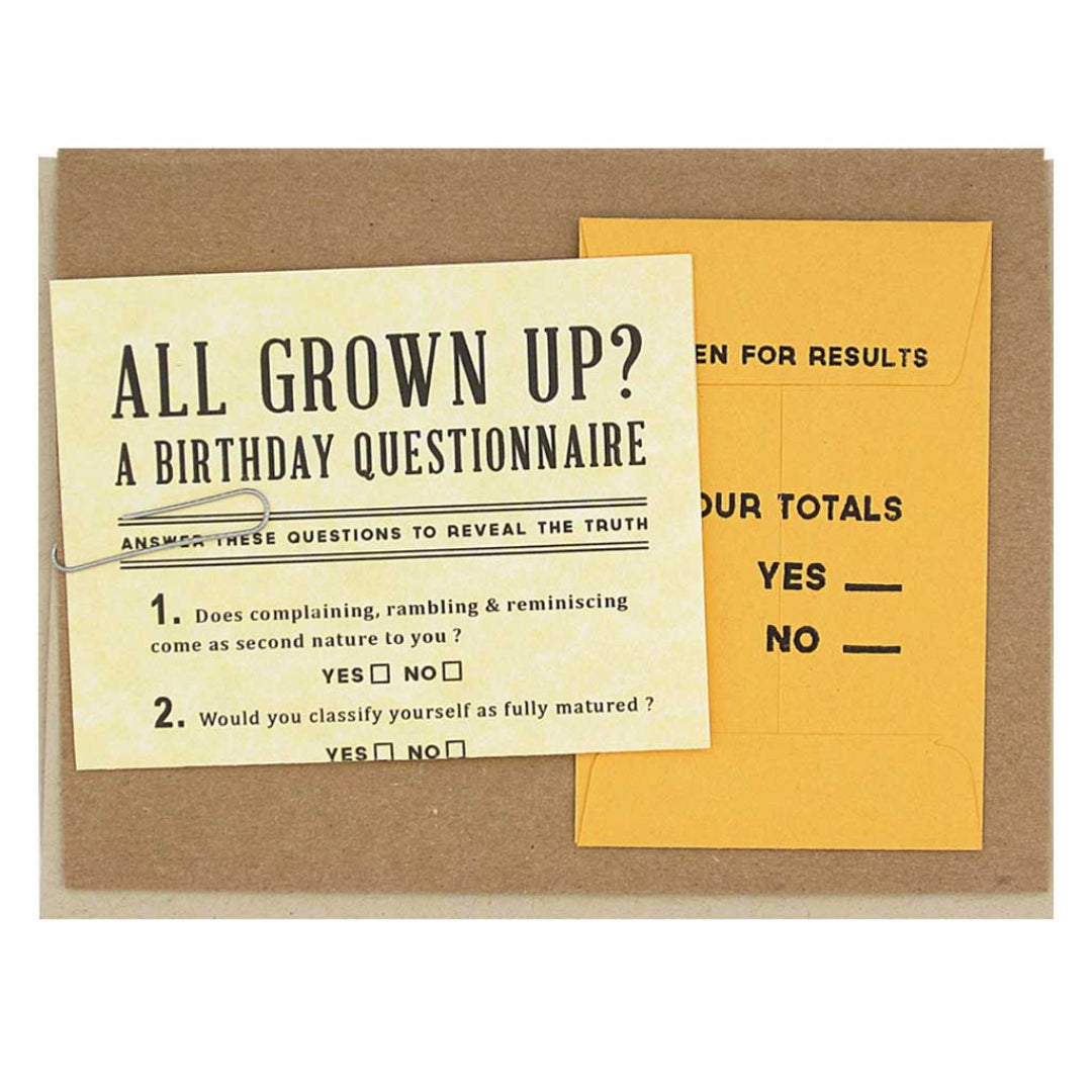 A kraft-colored greeting card featuring a yellow "Birthday Questionnaire" that asks, "ALL GROWN UP?" and prompts the recipient to "ANSWER THESE QUESTIONS TO REVEAL THE TRUTH." Two questions are visible: "1. Does complaining, rambling & reminiscing come as second nature to you?" and "2. Would you classify yourself as fully matured?". To the right, a small yellow envelope labeled "OPEN FOR RESULTS" has "YOUR TOTALS" and lines for "YES" and "NO" answers.