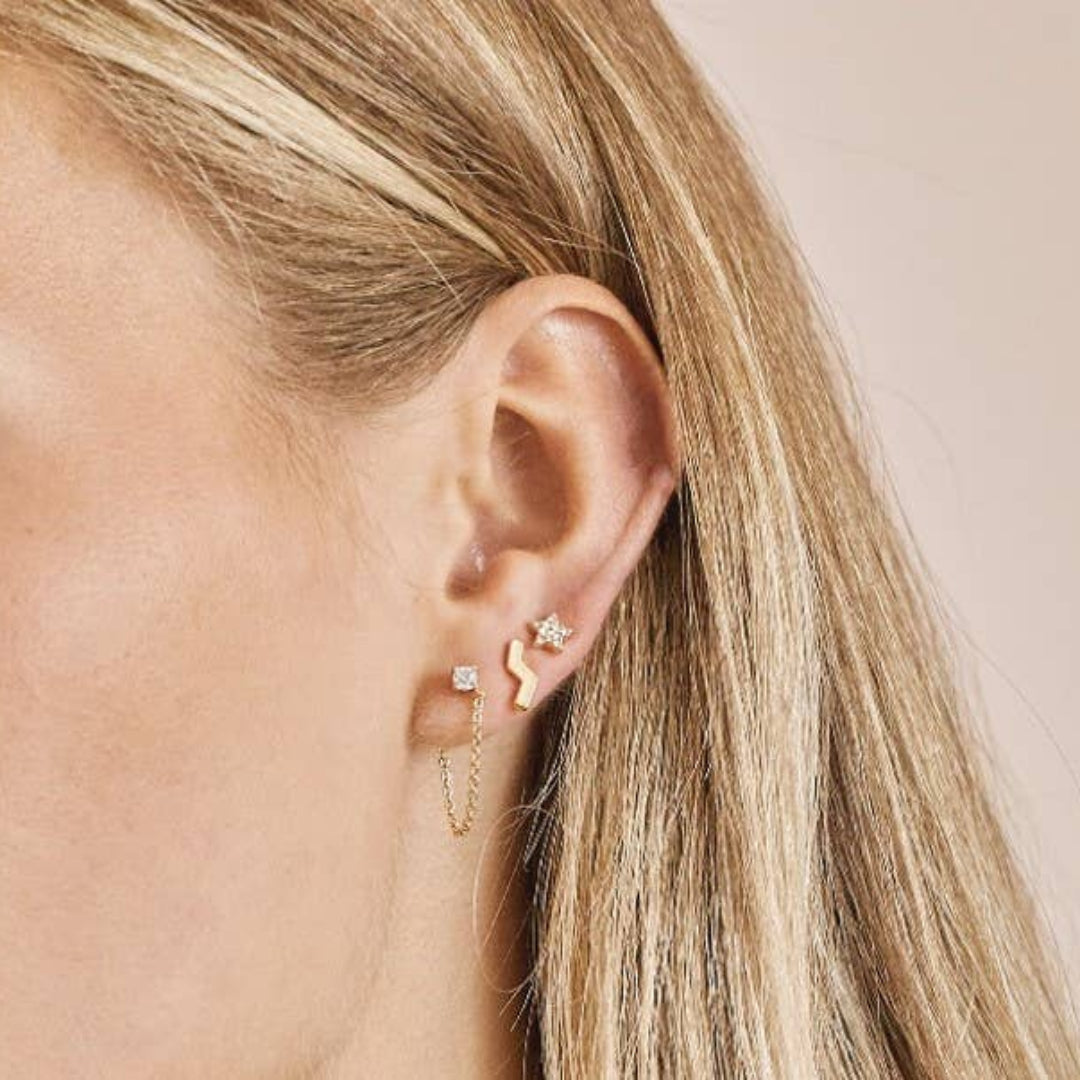 Close-up of an ear wearing gold earrings with a neutral background