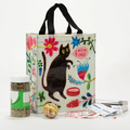 A reusable tote bag with a playful cat design. The bag is white with a black cat standing on its hind legs near a bowl of food. The text "CHOW TIME" is written above the cat, and the bag is decorated with colorful flowers and plants.