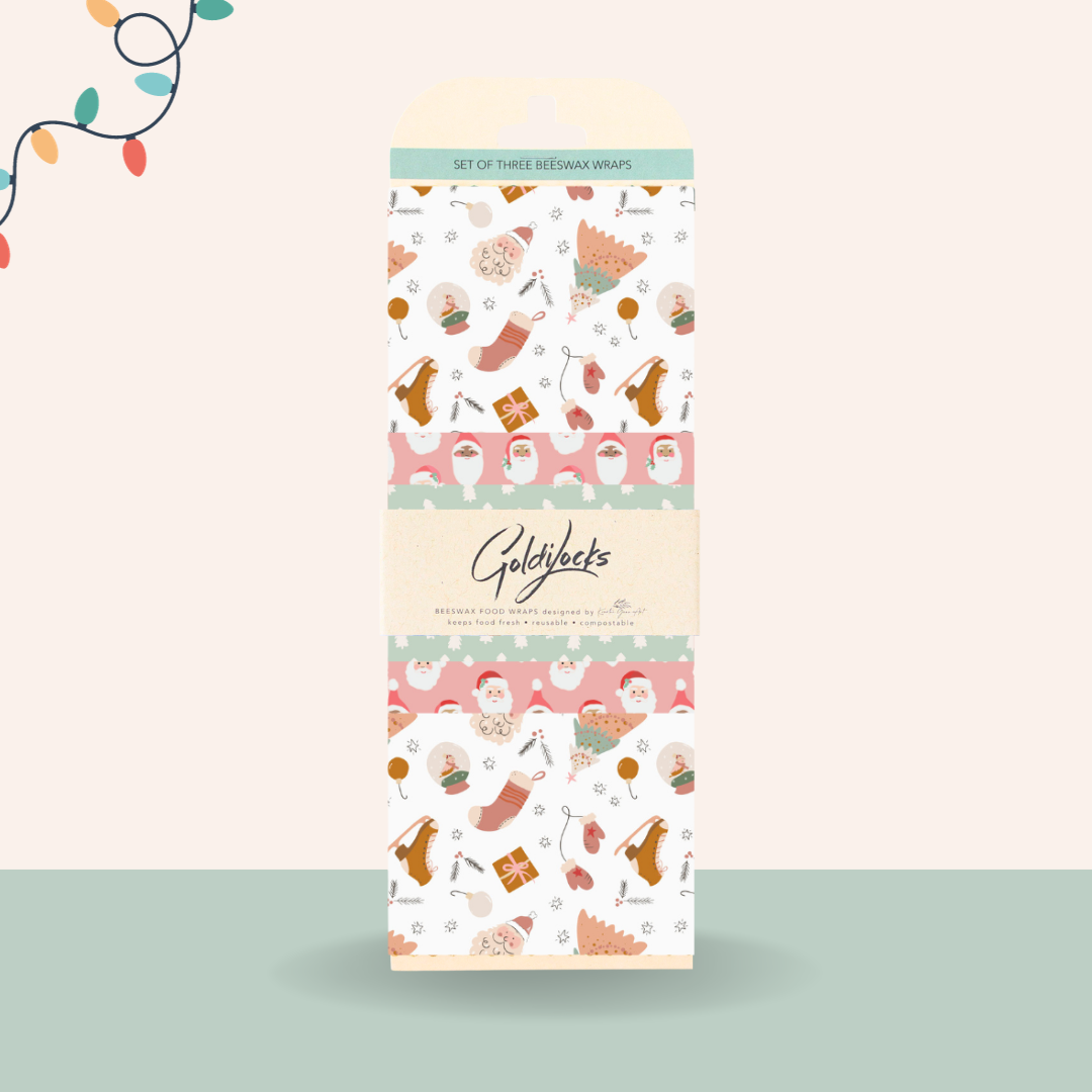 A set of three Christmas-themed beeswax food wraps. The wraps are packaged in a cardboard box with a festive design featuring Santa Claus, snowmen, and Christmas gifts. The brand name "Goldilocks" is printed on the box.