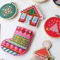 A collection of colorful Christmas ornaments made using plastic canvas. The ornaments include a gingerbread house, a Christmas stocking, Santa Claus, a snowman, a Christmas tree, and various ornaments.