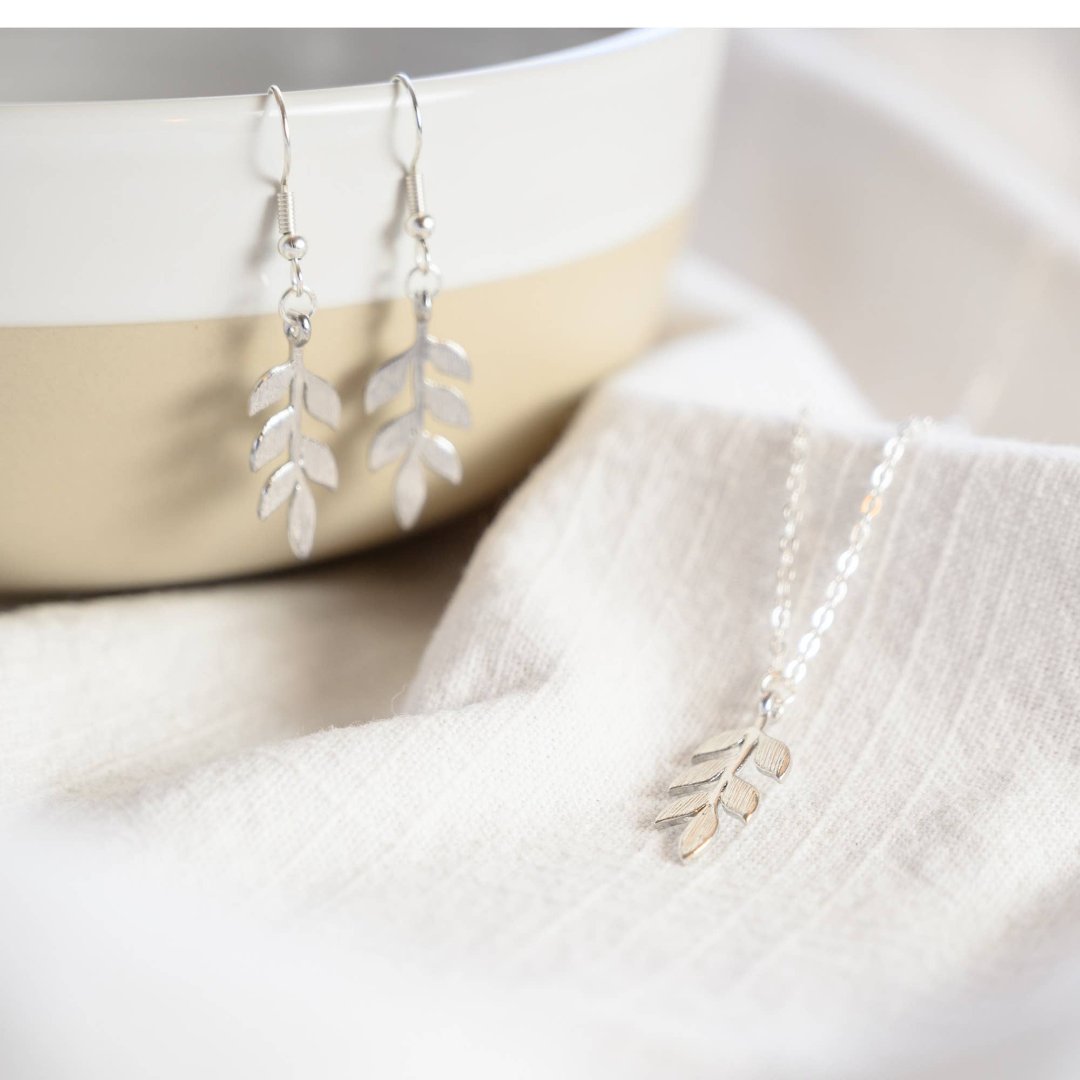 A silver necklace and earring set on a white card. The necklace features a silver leaf pendant, and the earrings are silver leaf-shaped drop earrings.