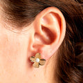 Gold flower-shaped earring with a pearl center worn by a person.