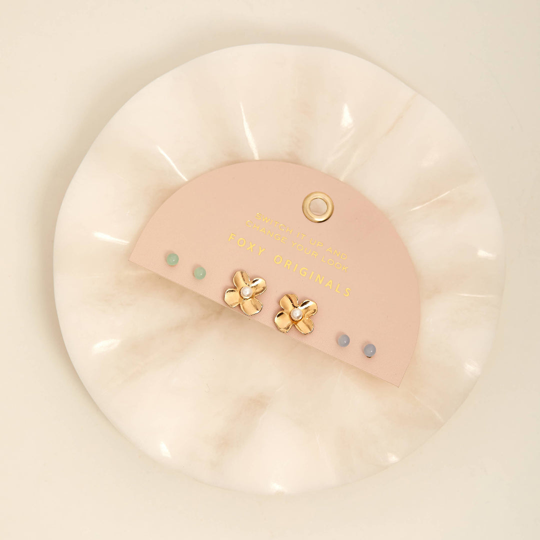 Pink earrings with gold accents in a clear plastic case on a light beige background