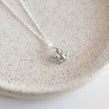 Silver necklace with a small pendant on a beige speckled plate