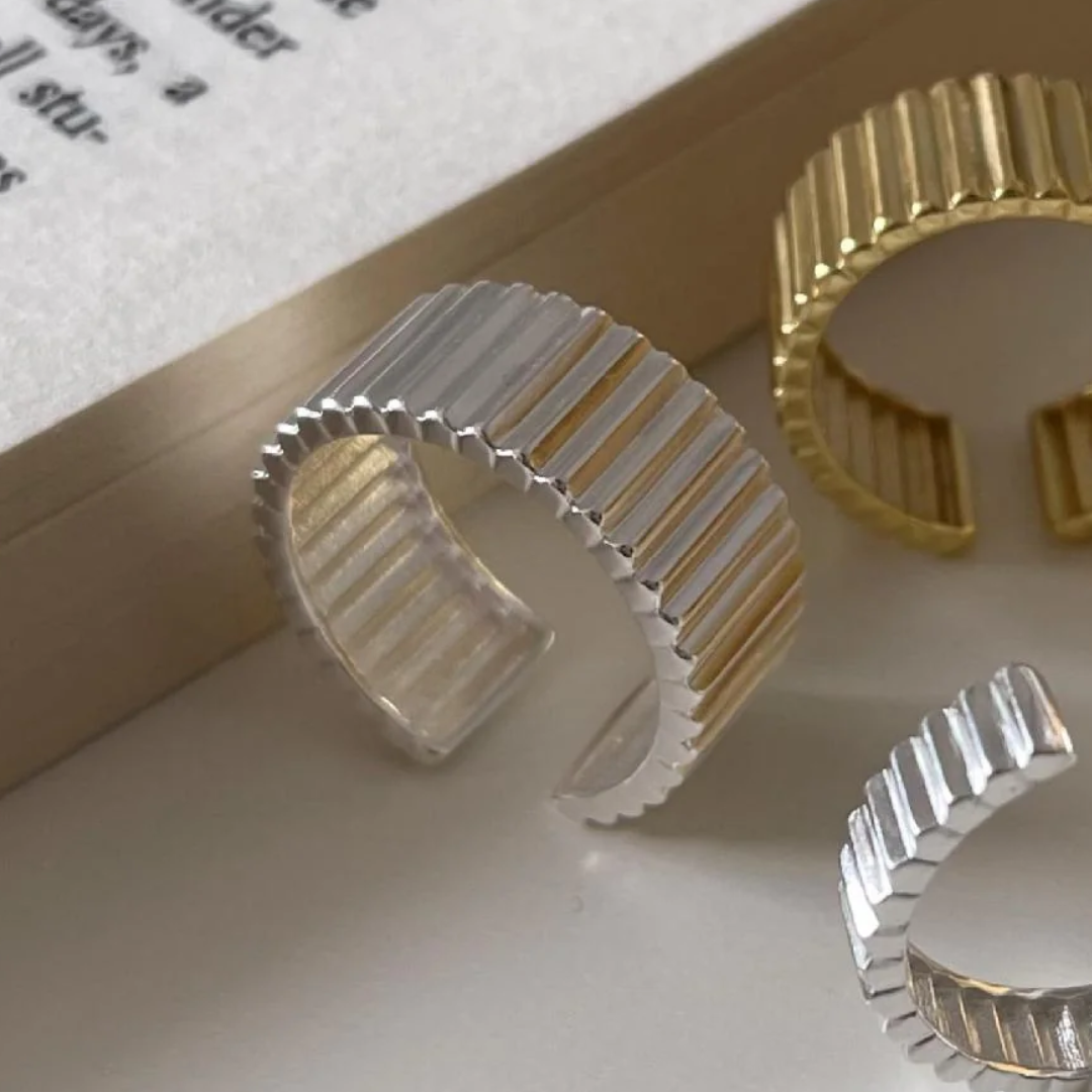 A wide band gear ring made with sterling silver, featuring a textured design resembling interlocking gears, worn on a person's thumb while holding a glass. This statement ring is available in Ottawa, Ontario, Canada.