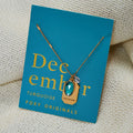 A gold necklace with a turquoise stone pendant. The pendant also has the word "FRIENDSHIP" engraved on it. The necklace is displayed on a blue card with the month "December" and the brand name "Foxy Originals."