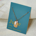 A gold necklace with a pearl stone pendant. The pendant also has the word "LOVE" engraved on it. The necklace is displayed on a blue card with the month "June" and the brand name "Foxy Originals."