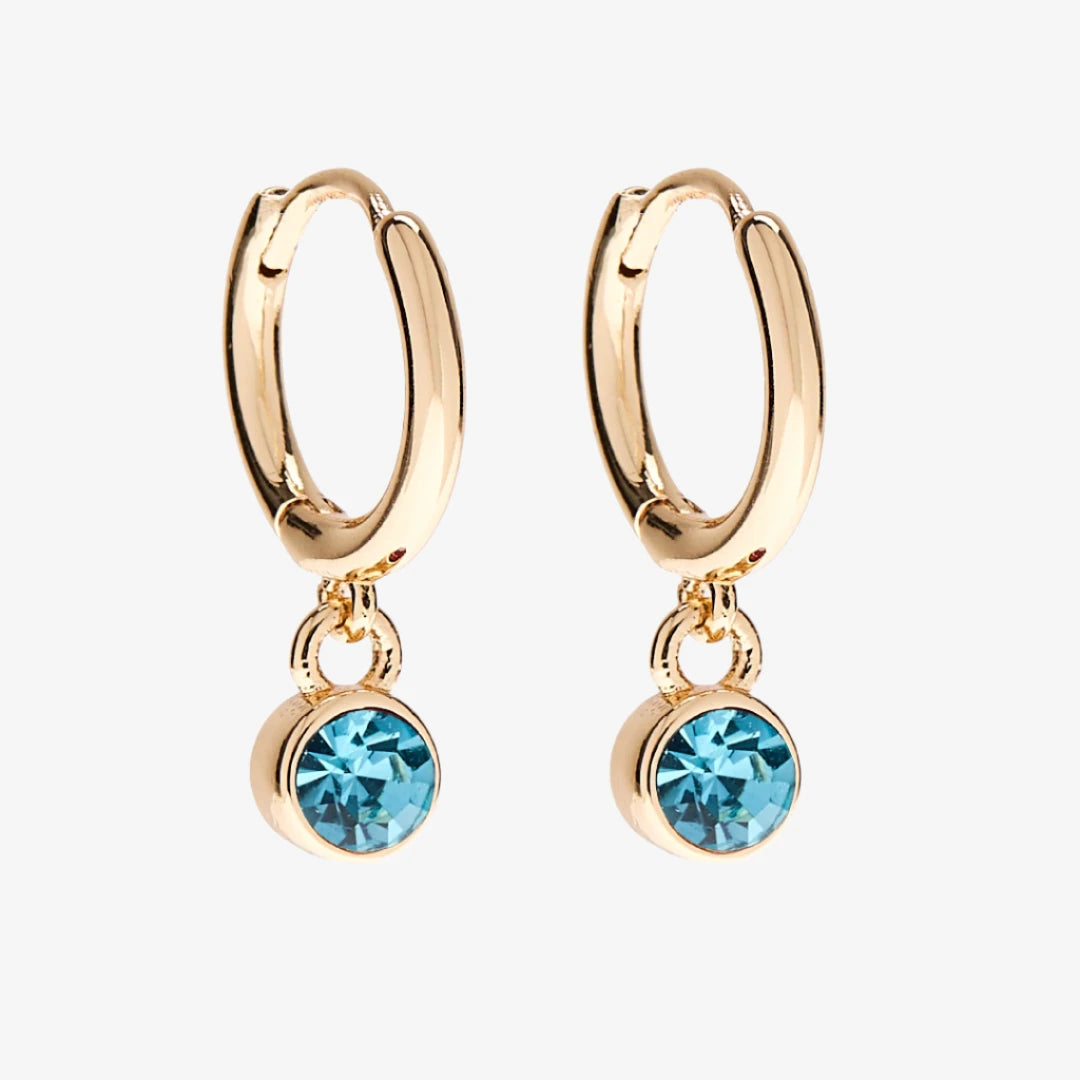 A set of three pairs of aquamarine earrings displayed on a light blue card. The set includes a pair of stud earrings, a pair of bar earrings with small aquamarine beads, and a pair of hoop earrings with dangling aquamarine stones. The card has the month "March" and the brand name "Foxy Originals."