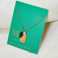 A gold necklace with an emerald stone pendant. The pendant also has the word "HOPE" engraved on it. The necklace is displayed on a green card with the month "May" and the brand name "Foxy Originals."