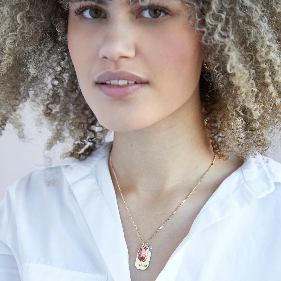 A gold necklace with an opal stone pendant. The pendant also has the word "HEALING" engraved on it. The necklace is displayed on a pink card with the month "October" and the brand name "Foxy Originals."