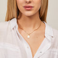 Woman wearing a gold necklace with a star pendant against a neutral background