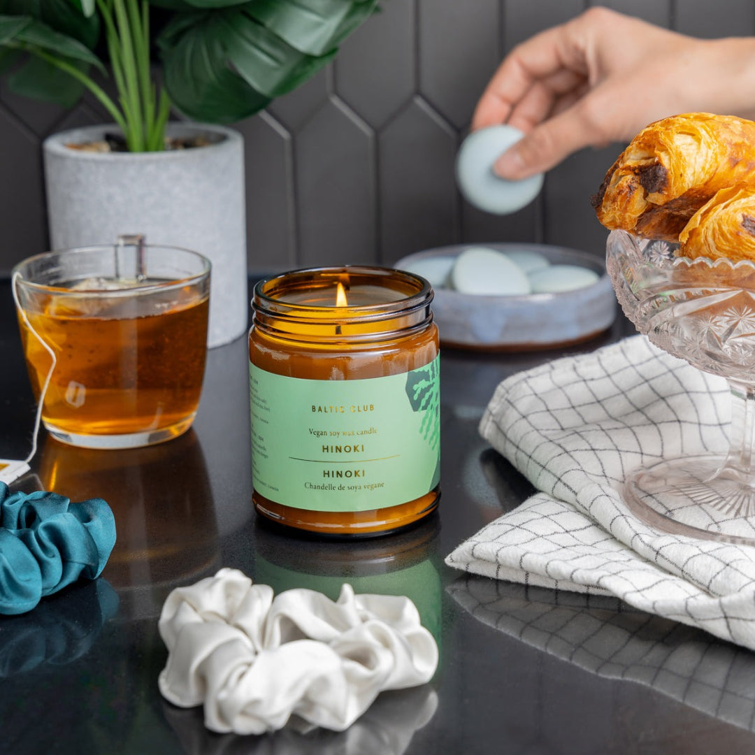 Candle with a green label on a table with tea, pastries, and decorative items.