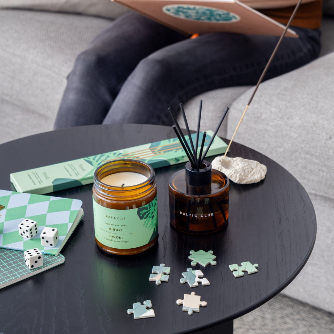 Candle, diffuser, and puzzle pieces on a table with a person sitting in the background.