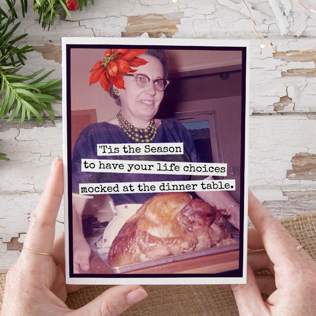 Person holding a card with a humorous message about life choices at the dinner table, with a roasted turkey on a table.