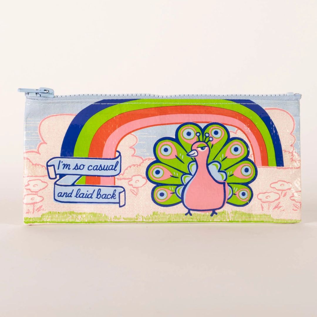 A rectangular light blue pencil case with a zipper, featuring a whimsical illustration of a pink peacock with an outstretched rainbow tail feathers. Above the peacock is a rainbow arc and a banner with the text "I'm so casual and laid back".