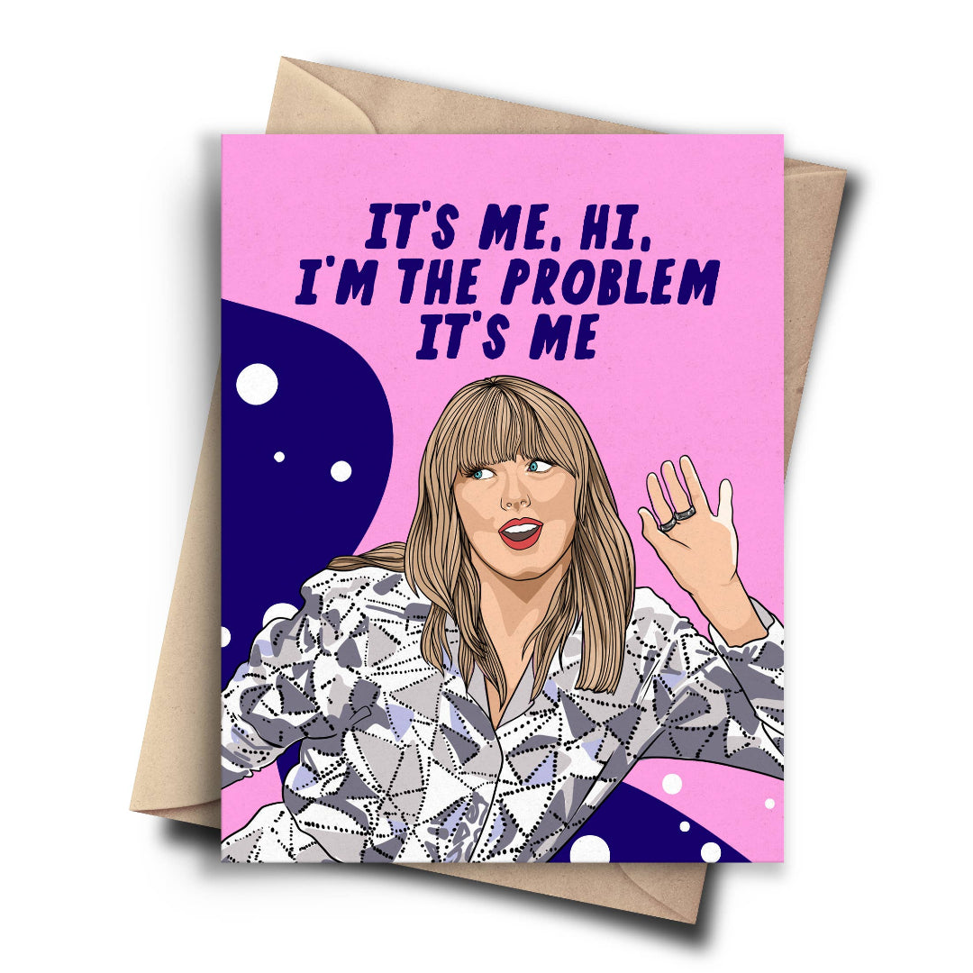 A humorous card featuring a cartoon drawing of Taylor Swift waving. The background is pink with white bubbles, and the text reads, "IT'S ME, HI. I'M THE PROBLEM IT'S ME." A brown kraft envelope is behind the card.