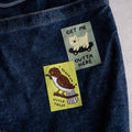 Two stickers on a denim surface, one with a dog and text, the other with a bird and text.