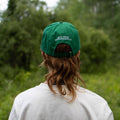 Person wearing a green cap with text in a natural setting