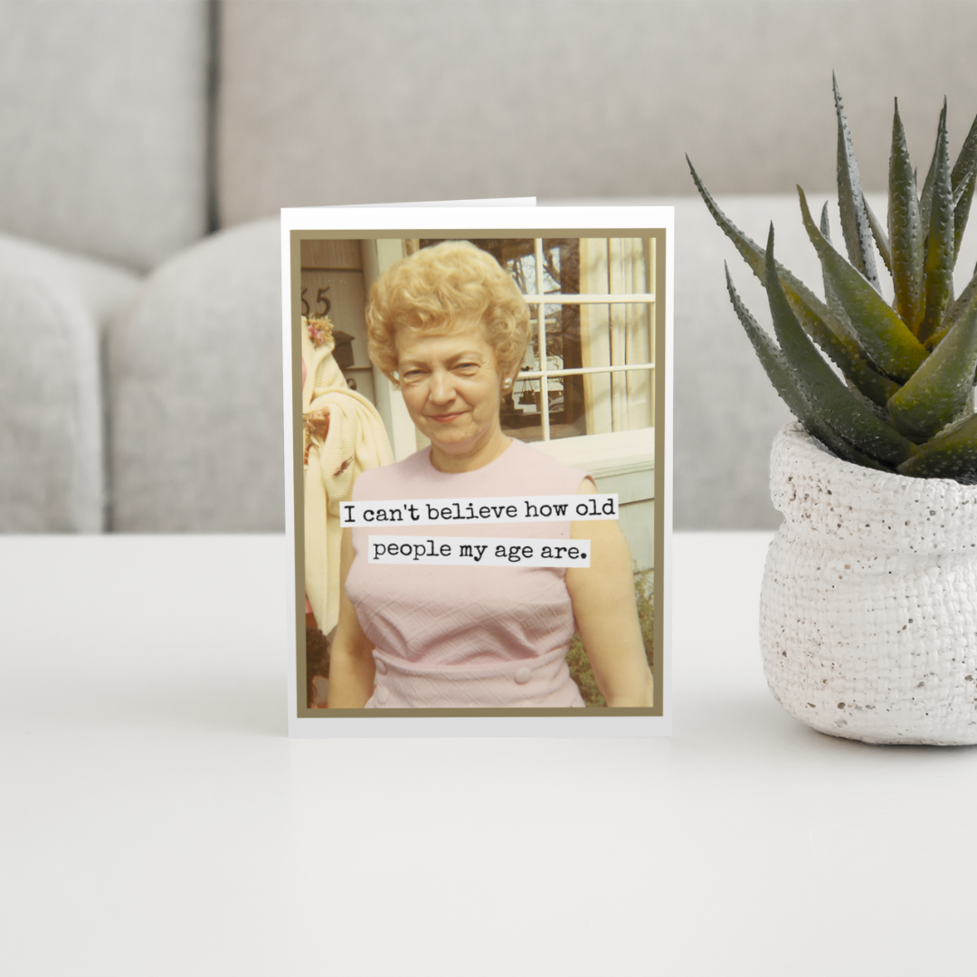 Card with a photo of an elderly woman and humorous text on a surface with a plant in the background