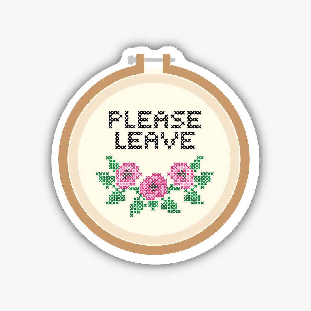 A circular sticker designed to look like an embroidery hoop, holding a piece of cream-coloured fabric. Cross-stitched in black on the fabric are the words "PLEASE LEAVE". Below the text, there's a cross-stitched floral design with three pink flowers and green leaves.