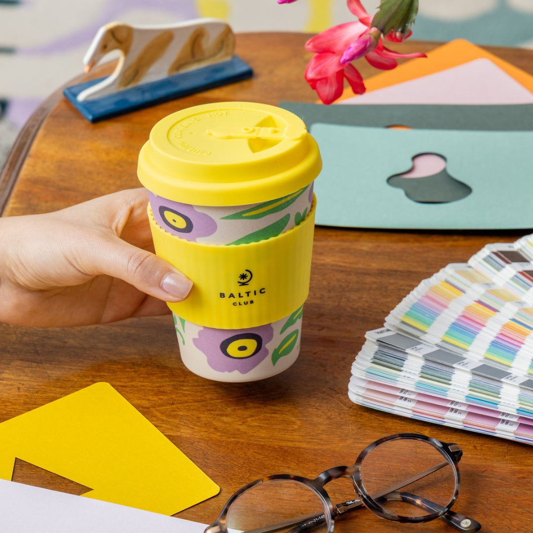 Hand holding a yellow coffee cup with floral design on a wooden table.