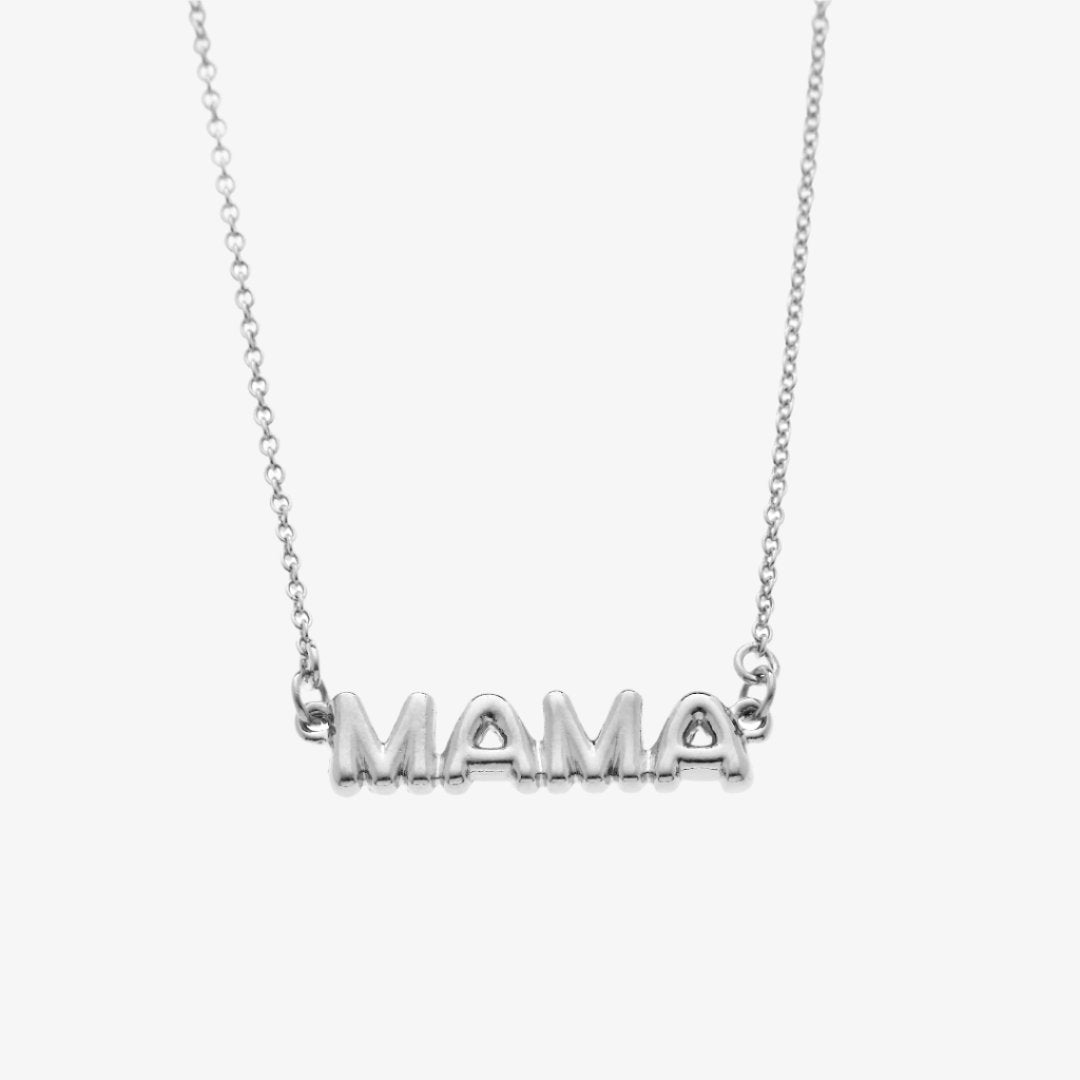 A silver necklace on a pink background. The necklace features a silver pendant with the word "MAMA" in bold letters. The text "COOL MAMA FOREVER" is printed on the background card, along with the brand name "Foxy Originals."