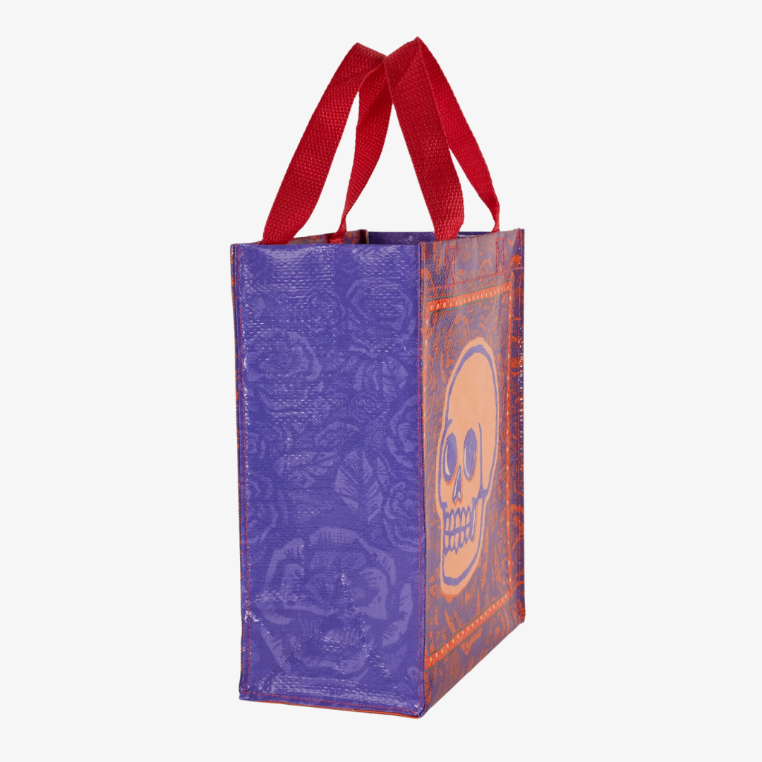 A reusable tote bag with a skull and roses design. The bag is purple with a large orange skull in the center. The skull is surrounded by red roses and has a black outline. The bag has red handles.