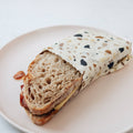 Half-eaten sandwich wrapped in a patterned paper on a white plate