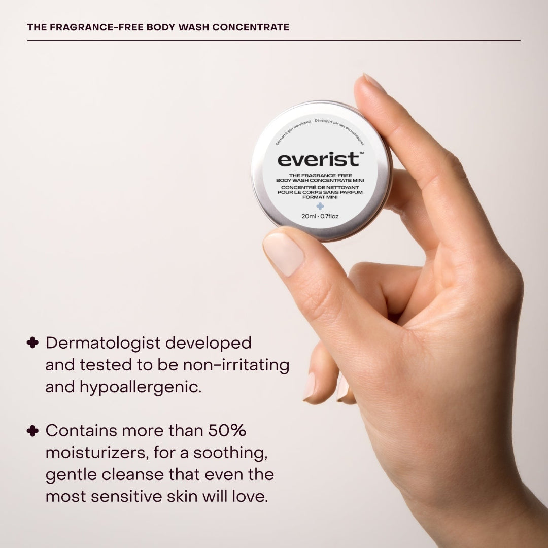 A small, open, silver metal tin of Everist's "The Fragrance-Free Body Wash Concentrate Travel Mini," revealing a white solid product inside. The tin's lid is propped against the base, and text on the side indicates it's dermatologist-developed and contains 20ml of product.